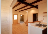 白い壁と天井に、こげ茶の化粧梁がよく映えるキッチンからリビングルームにかけての空間